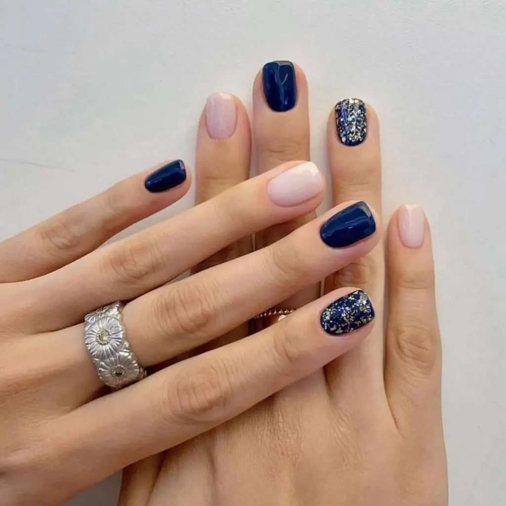 Navy blue and nude pink nails with silver glitter accent on short nails