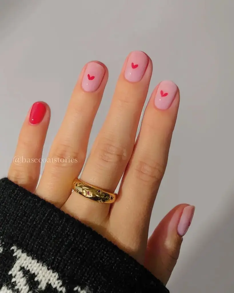 Matte pink short valentine day nails with red heart accents and red accent nail, gold ring accessory