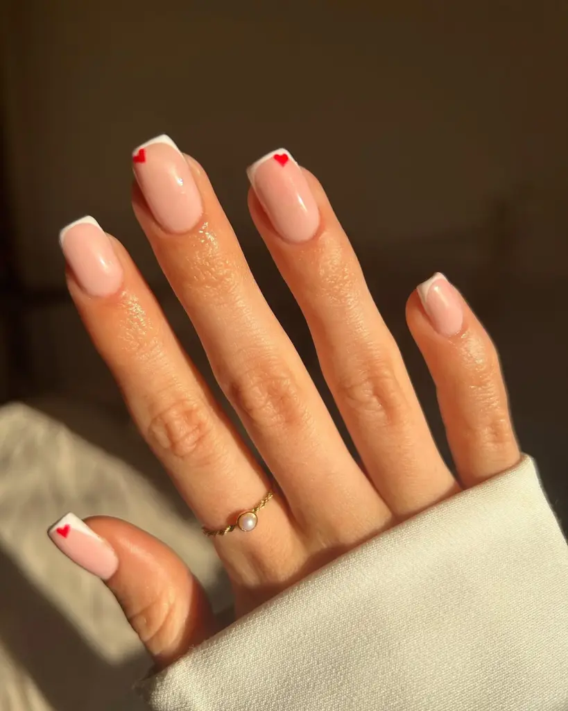 Short nude valentine’s day nails with white french tips and tiny red heart accent