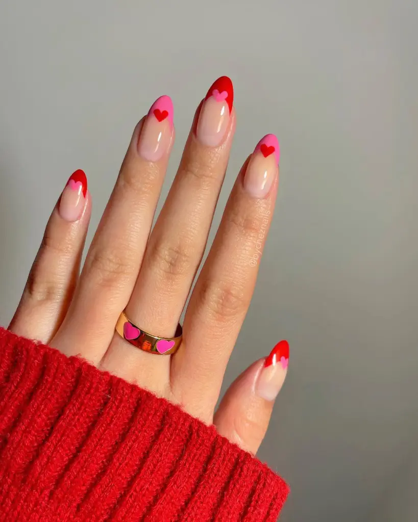 Valentine's Day French manicure with alternating pink and red heart-shaped tips on sheer pink base