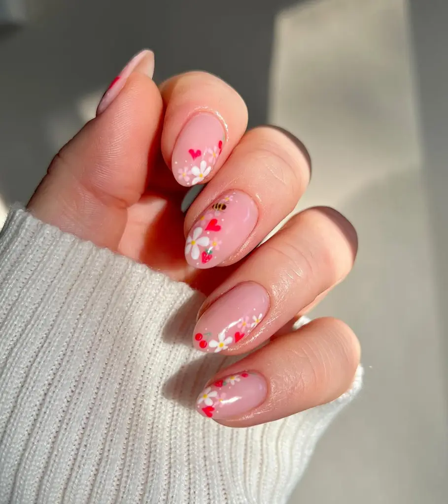 Almond shaped nails with sheer pink base, tiny red hearts and small white flower accents scattered across tips