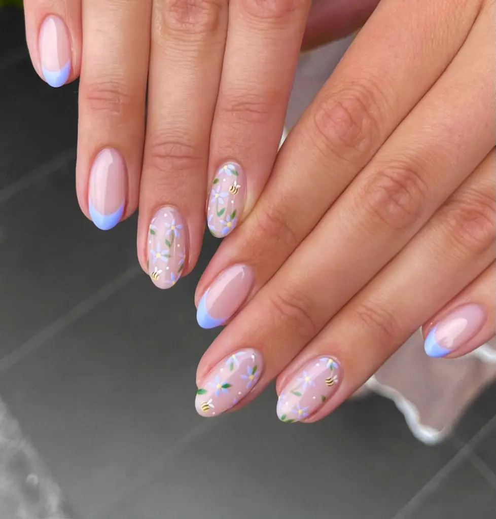 Almond spring nails with pink base, blue French tips, and pressed flower nail art with bee details