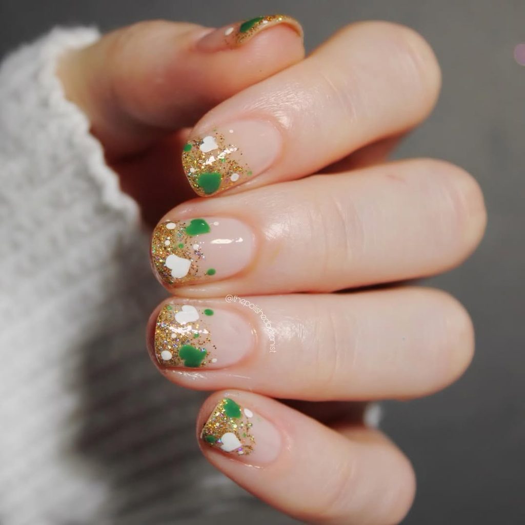  St Patrick's Day short nails with nude base, gold glitter tips and small green accents
