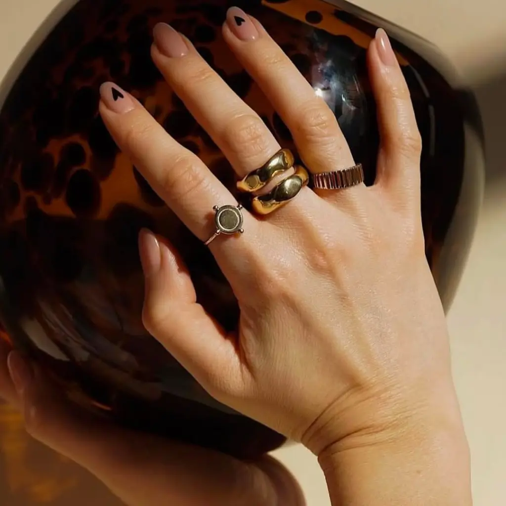 Medium almond nails with nude pink polish and two black heart accents