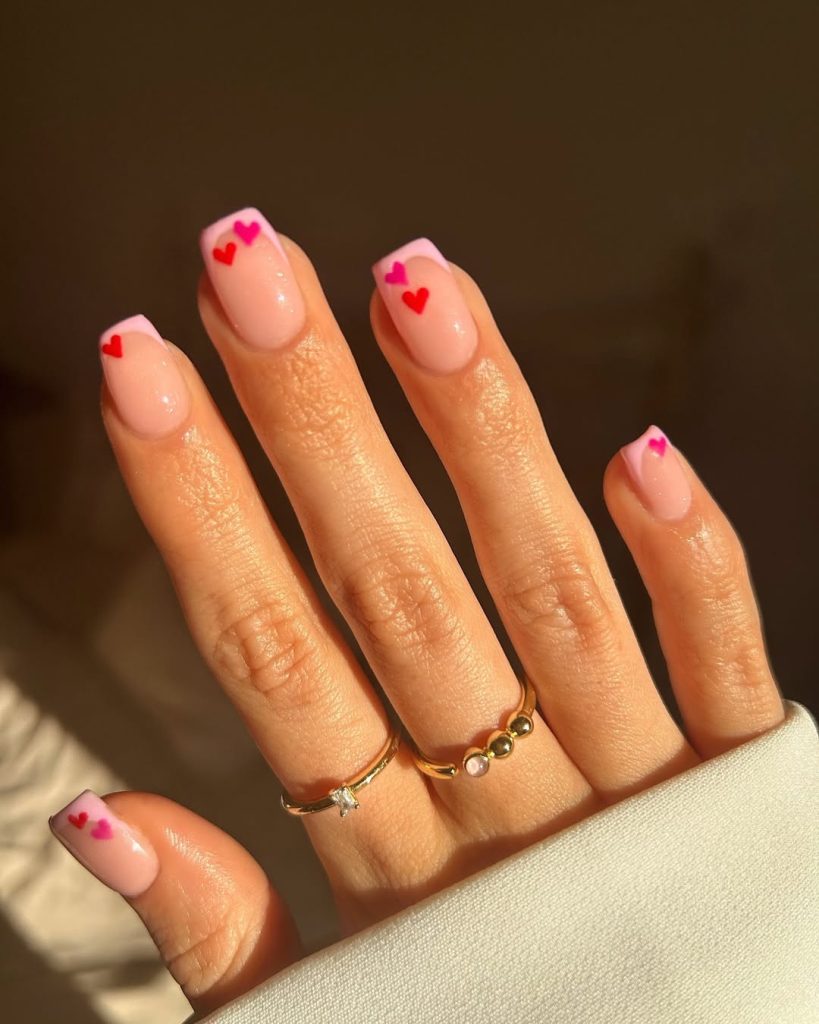 Natural nails with pink French tips and tiny red hearts along tip line
