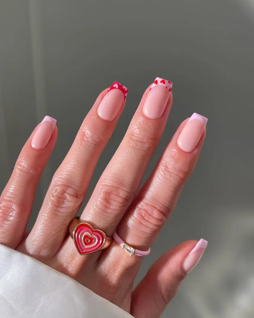Light pink French tips with red heart accents on natural nails