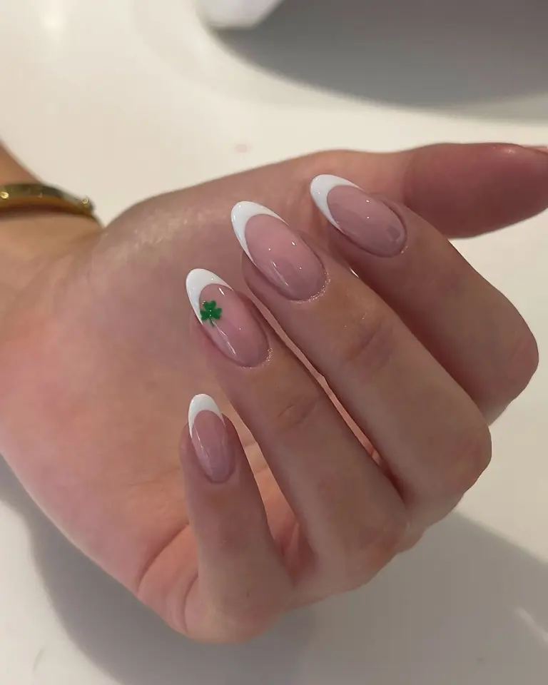 Long almond nails with white French tips and small green shamrock accent nail