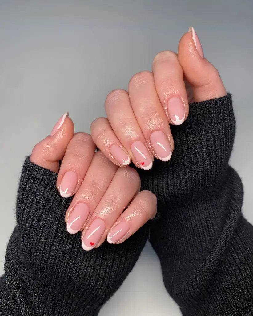 Soft pink French tips with tiny red heart accent and almond shape