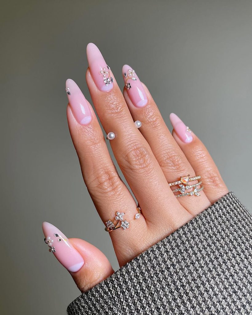 Pink almond nails with rhinestone flower details and pearl accents
