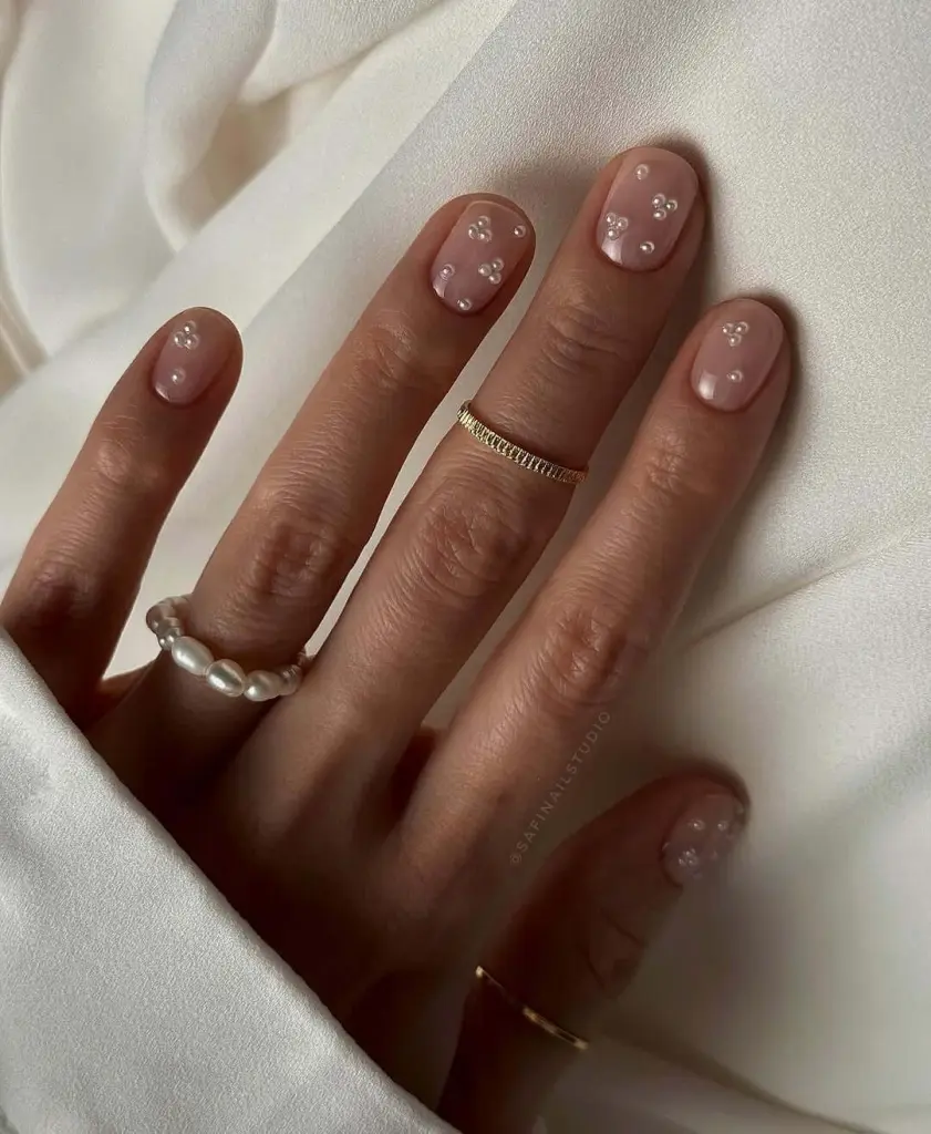 Nude pink nails with scattered pearl crystal accents
