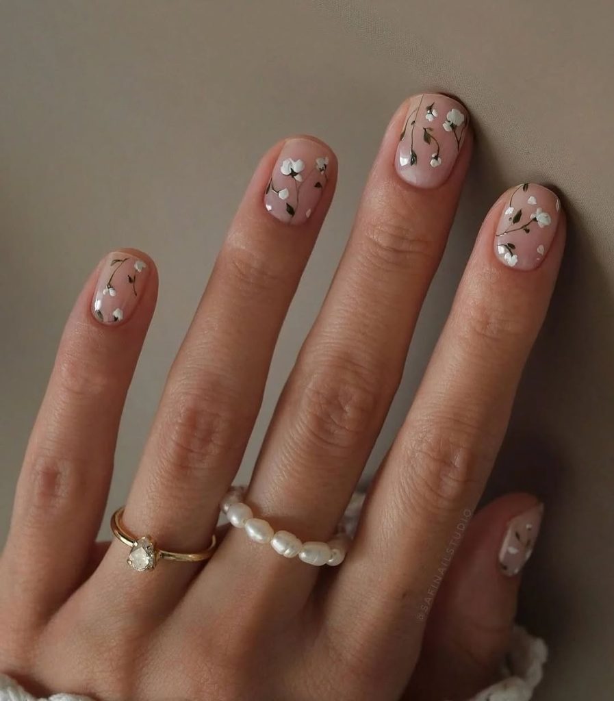 Short spring nails with nude pink base and white daisy pattern with green stems