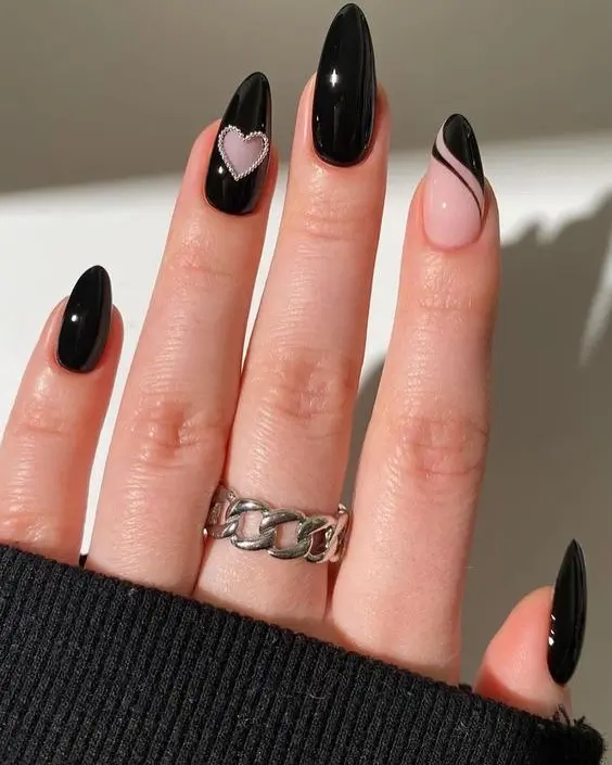 Black almond nails with nude accent nail and crystal heart detail

