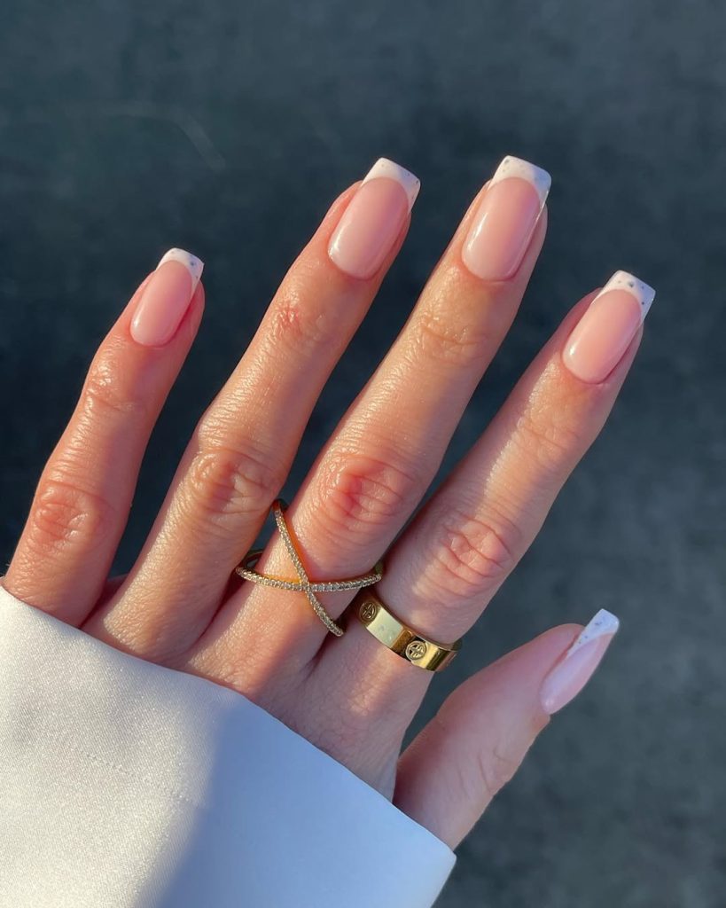 Elegant long square nails with sheer nude base and speckled white french tips with gold accents