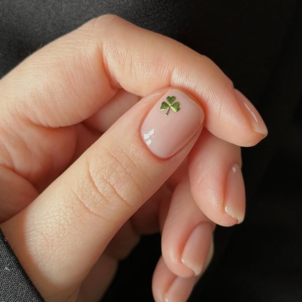 Short natural nails with sheer pink base and small green shamrock decal