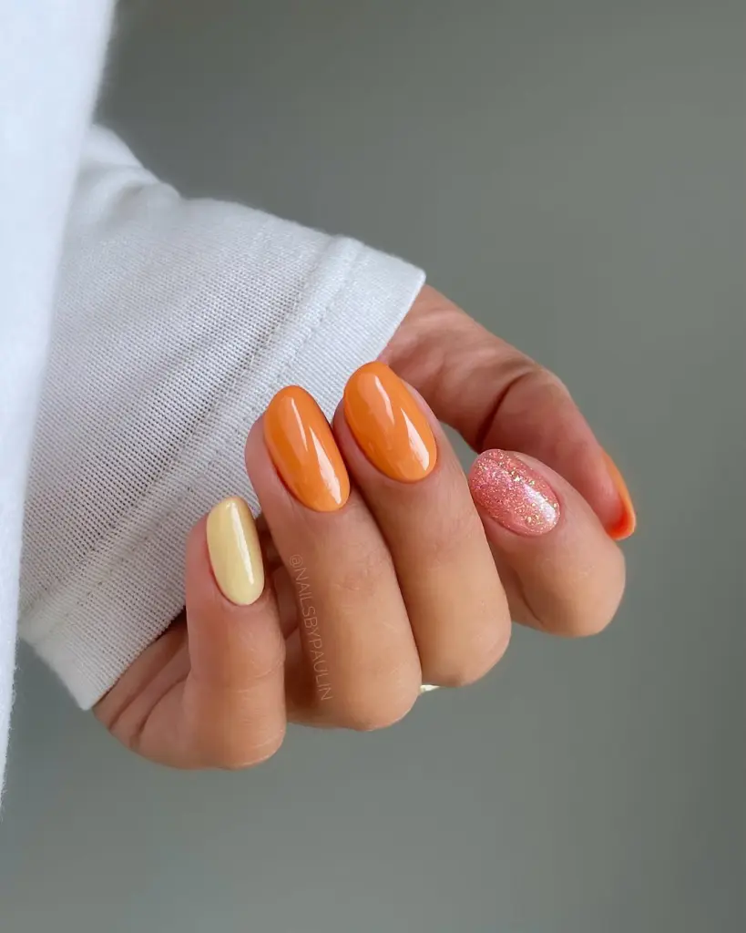 Short almond spring nails with orange and yellow polish, plus glitter pink accent nail