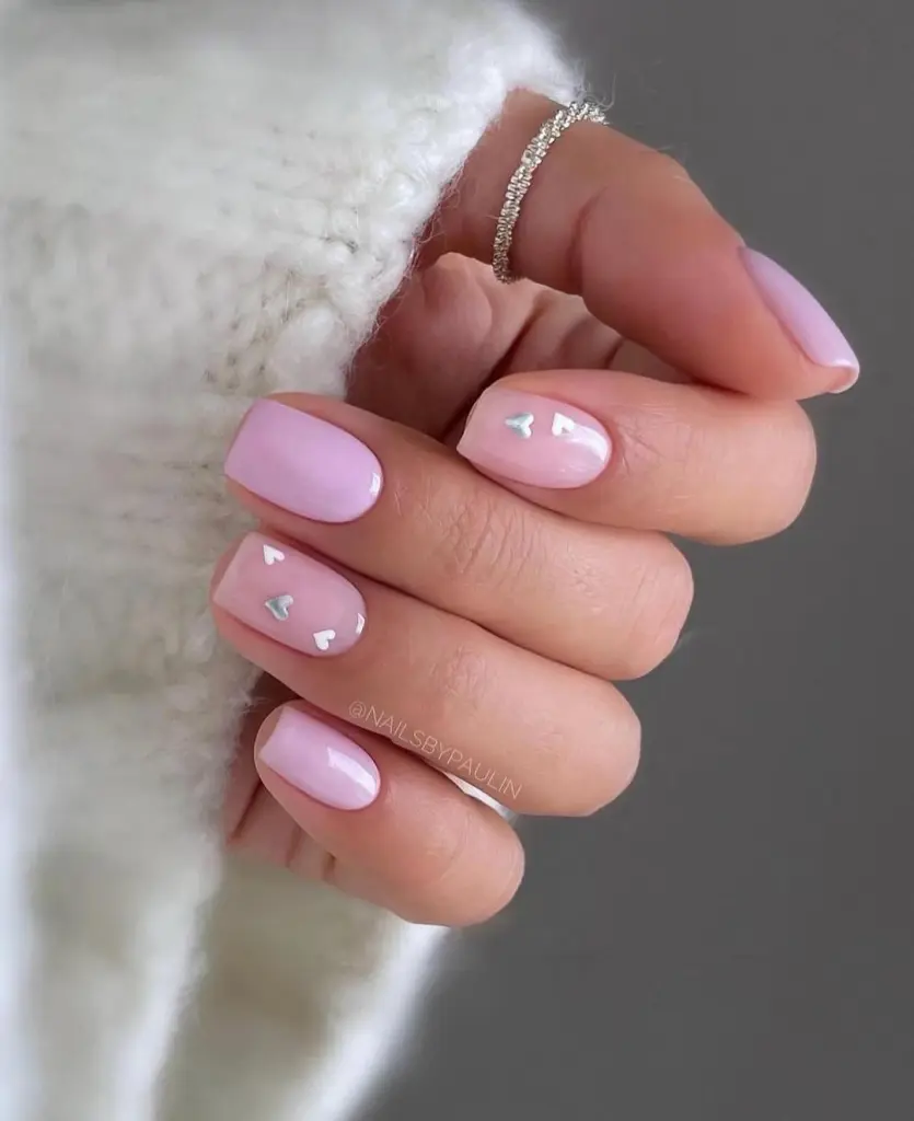 Short pink and sheer pink nails with iridescent heart accents and rhinestone ring accessory