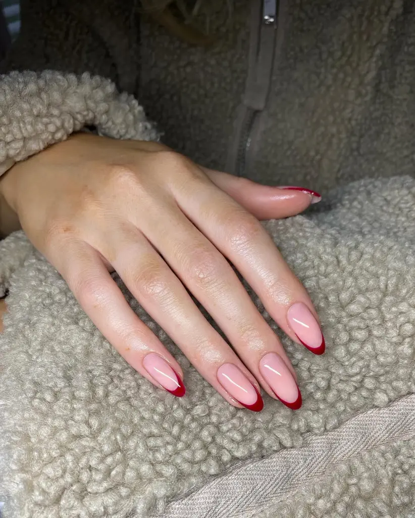 Sheer pink nails with cherry red French tips and almond shape