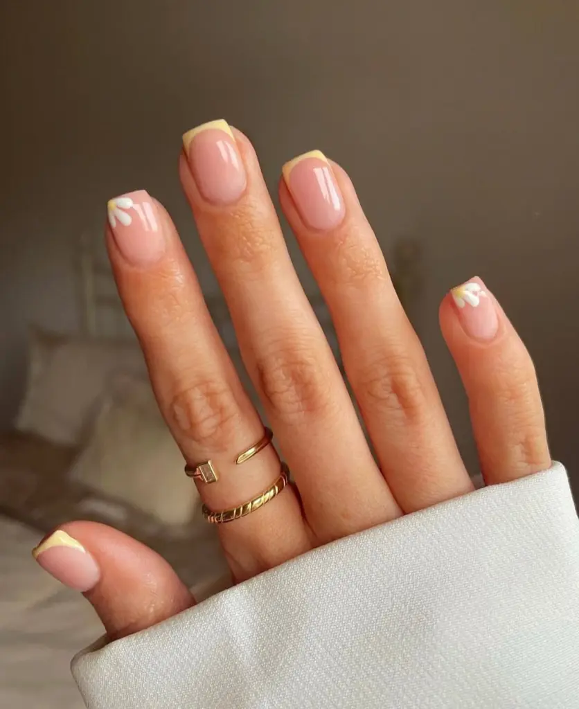 Spring  nails with sheer pink base, yellow french tips and white daisy details
