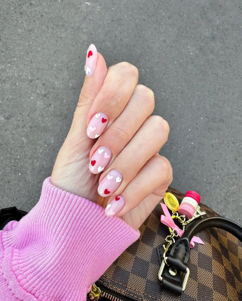 Milky white nails with tiny red hearts and round shape
