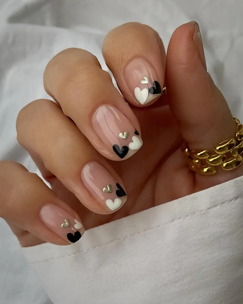 Short sheer nude nails with black and white heart designs and pearl accents