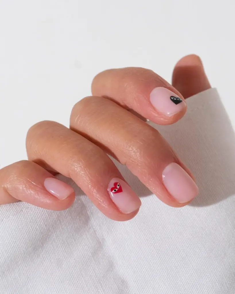 Short pink nails with micro heart designs and black accents
