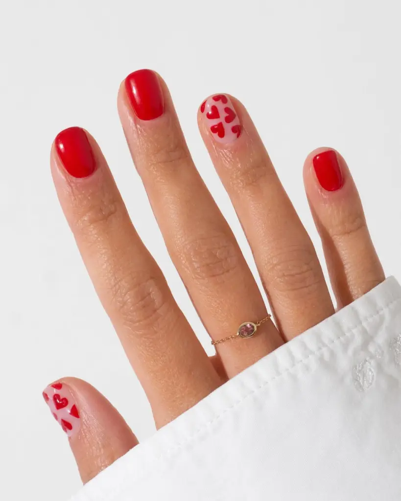 Red nails with sheer negative space hearts and solid red accent nails
