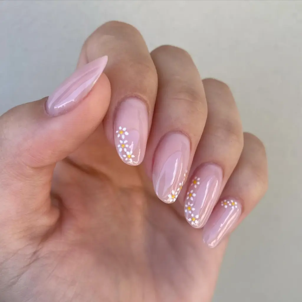 Short almond nails with sheer pink base and scattered white daisy pattern on tips