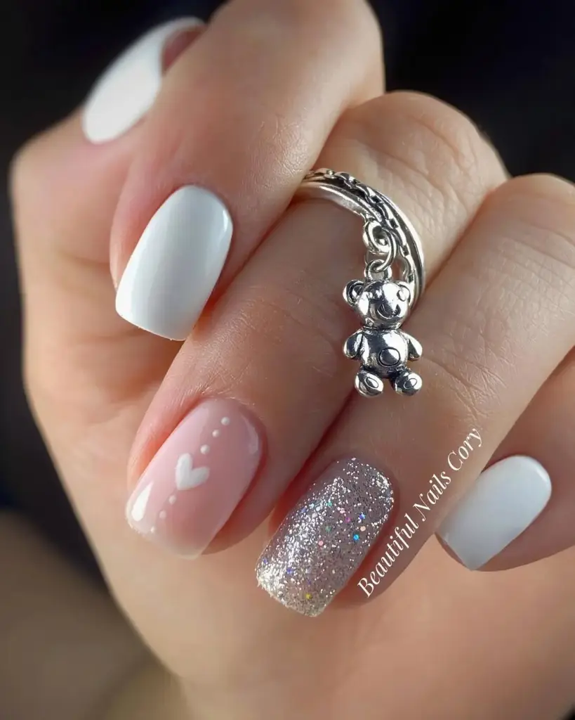 Short white and pink nails with silver glitter accent and heart designs
