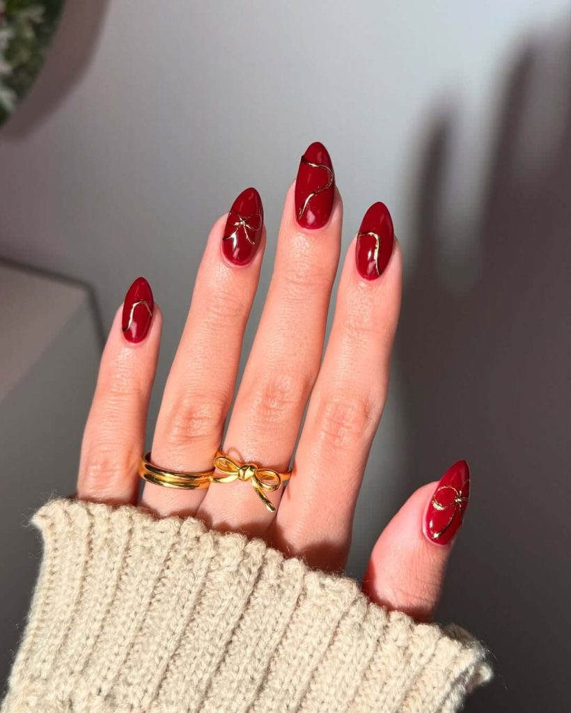Burgundy almond nails with gold curved accents