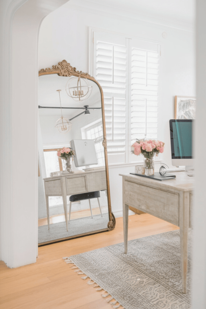 An elegantly designed office with a large ornate mirror leaning against a white wall