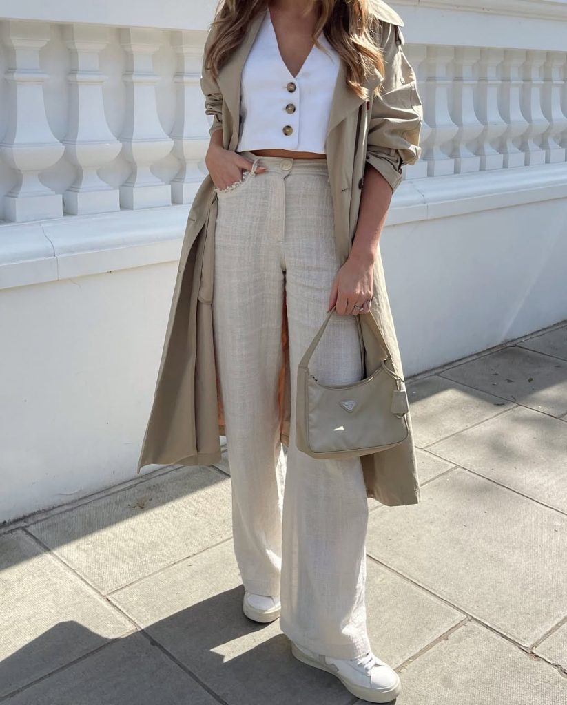 Spring neutral classy outfit with white button vest, wide leg linen pants, beige trench coat, white sneakers, and structured shoulder bag