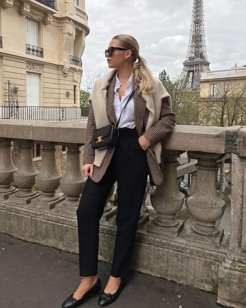 Classy outfit with brown houndstooth blazer, white button-down shirt, black tailored trousers, cream sweater draped over shoulders, black flats and leather crossbody bag