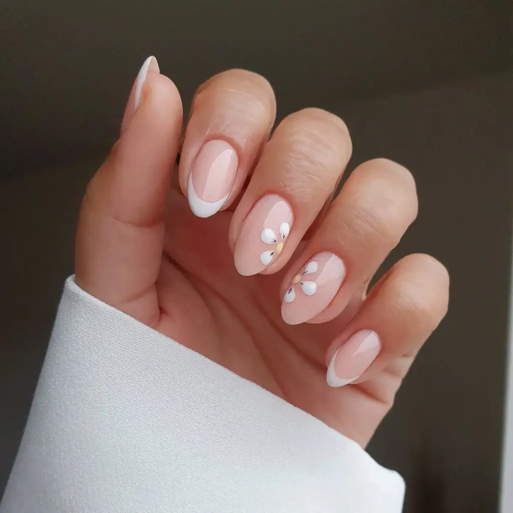 Almond shaped nude nails with classic white French tips and delicate daisy flower accents creating refined spring old money elegance