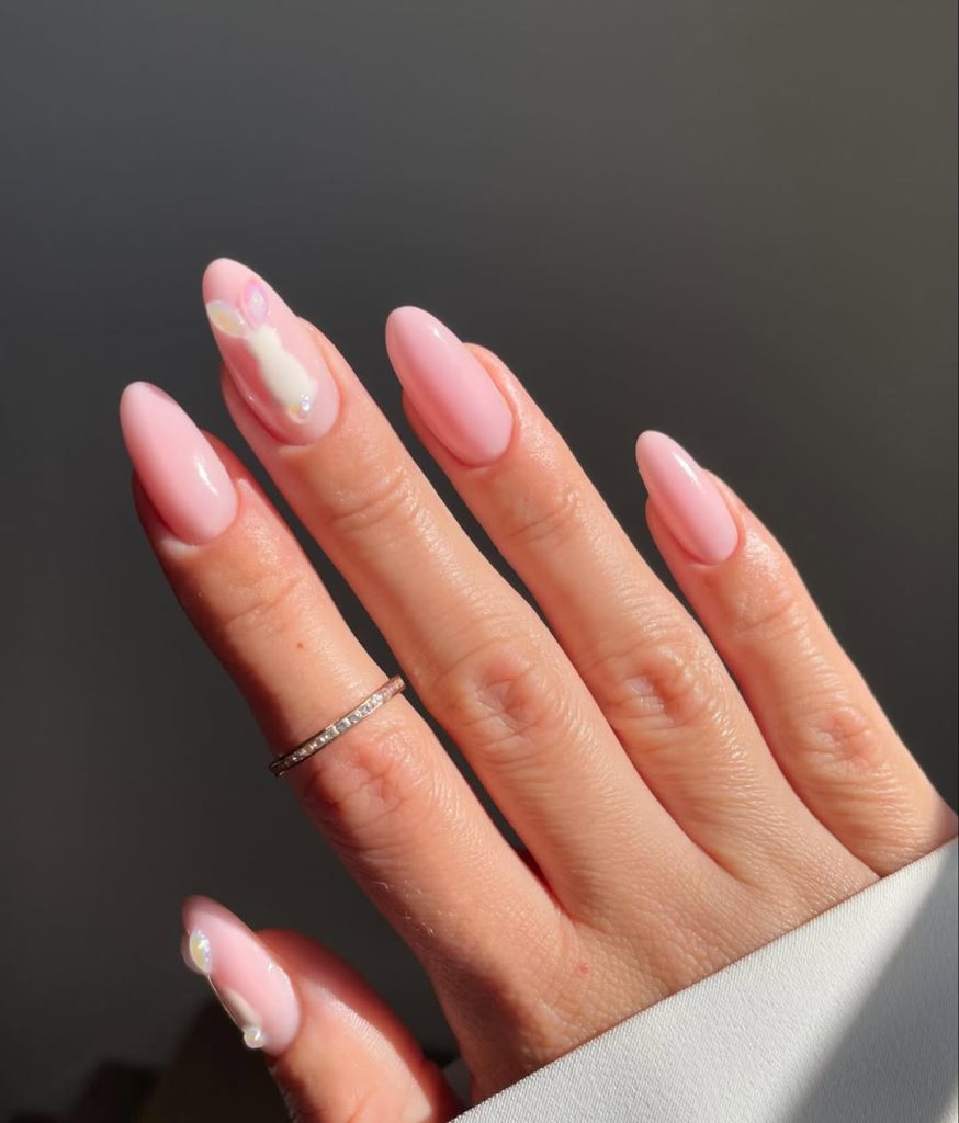 Almond-shaped pale pink nails with an accent nail featuring a delicate white bunny design and crystal embellishments, creating an elegant Easter-inspired manicure
