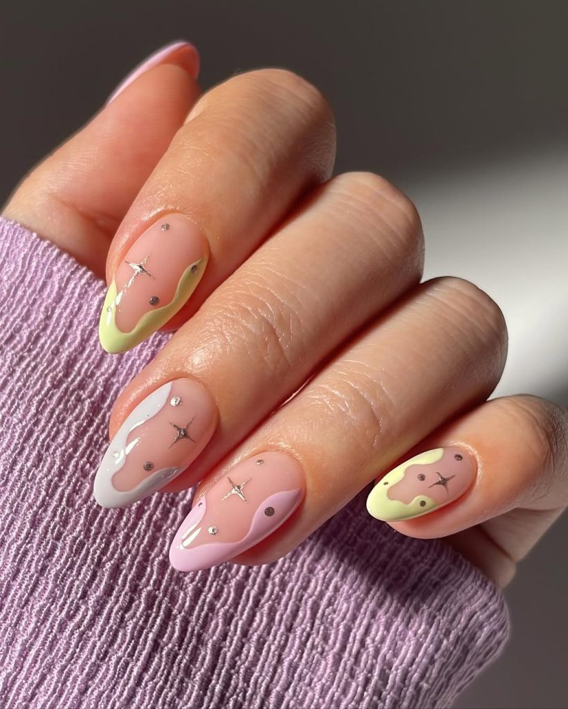 Almond-shaped nails with pink base featuring abstract pastel drips in white, yellow, and pink with metallic accents