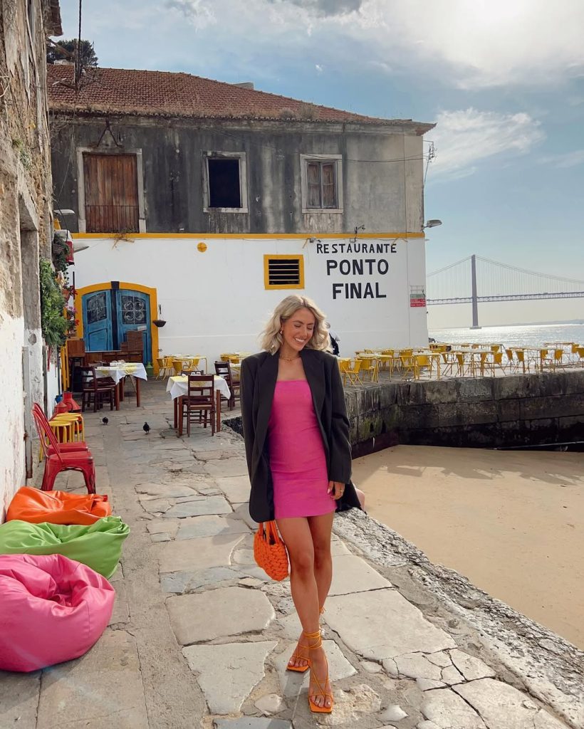 Woman in pink mini dress and black oversized blazer with orange accessories
