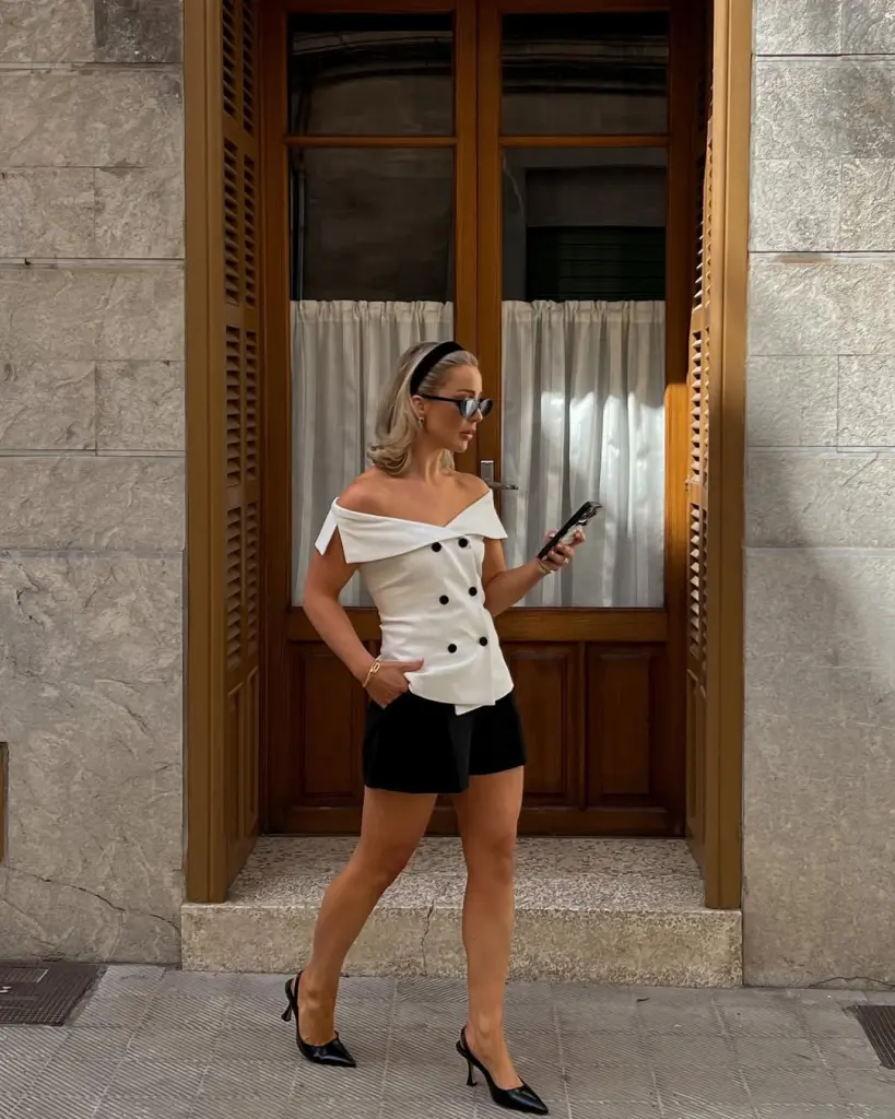 Old money outfit with white off-shoulder double-breasted top, black tailored shorts, black slingback heels and black headband