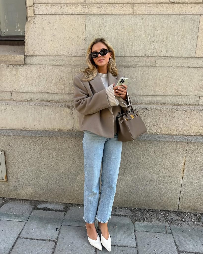 Elegant spring outfit with taupe cropped coat, cream sweater, straight leg jeans, white kitten heels and taupe structured bag
