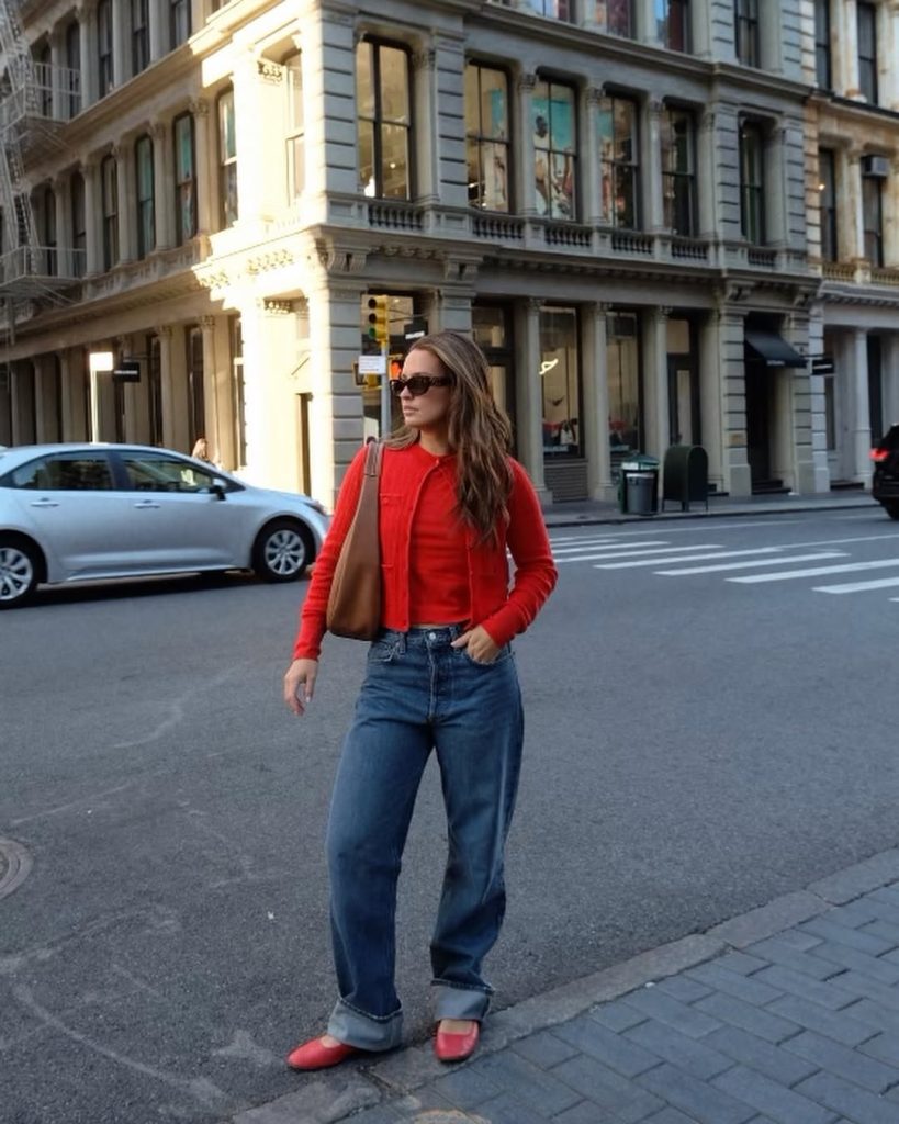 Casual spring outfit featuring a vibrant red fitted cardigan, high-waisted relaxed straight-leg jeans with cuffed hem, matching red ballet flats, brown leather shoulder bag, and oversized sunglasses
