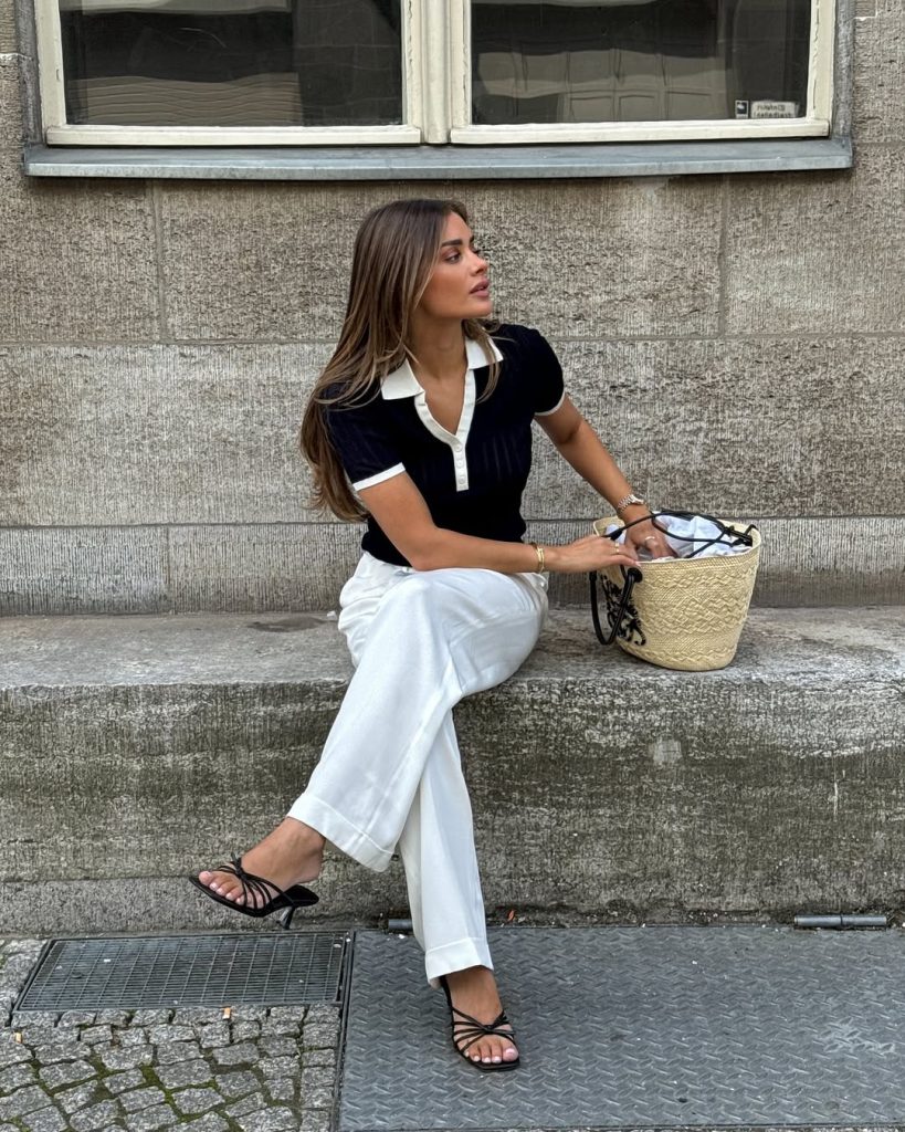Mediterranean summer outfit with navy and white collared top, white wide-leg trousers, black minimal sandals and natural straw tote bag