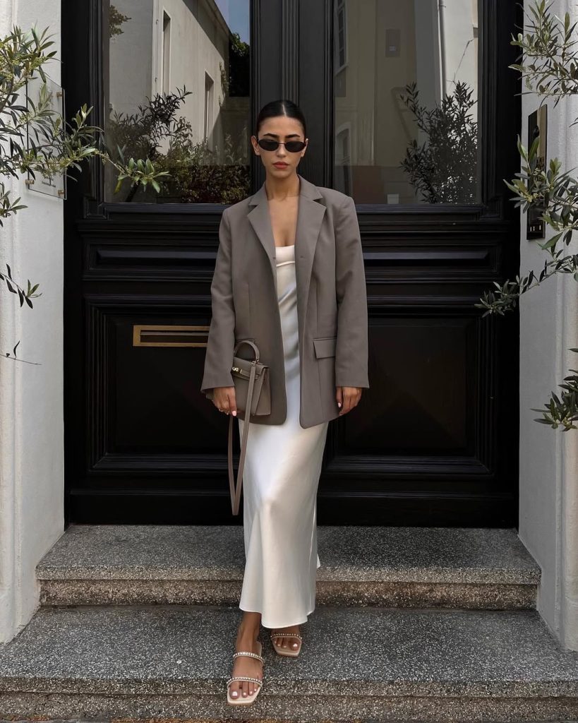 Woman in grey blazer and white silk maxi dress with crystal slides
