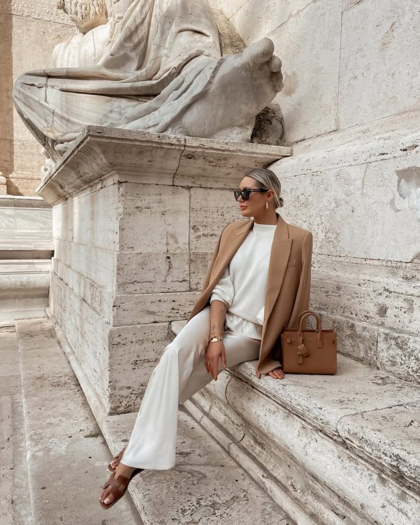 Classy  outfit with camel blazer, white knit top and matching wide-leg pants, tan mini tote bag, gold jewelry and black oversized sunglasses
