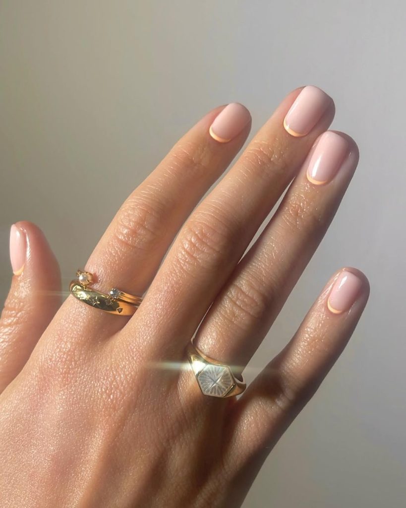 Short sheer pink nails with delicate peach rim detailing creating an elegant spring old money aesthetic
