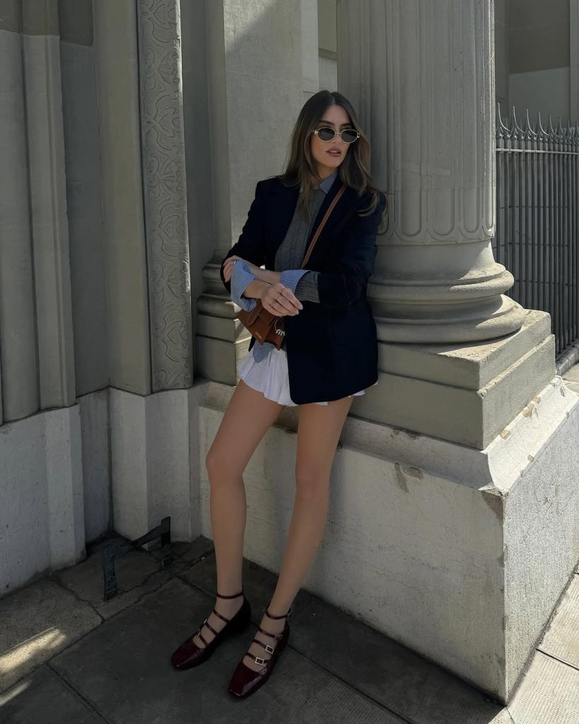 Preppy spring outfit with navy blazer, striped button down, white tennis skirt and burgundy strap flats

