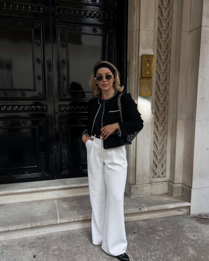 Luxury designer outfit with black boucle jacket with white trim, white wide-leg trousers, black headband, small round sunglasses and quilted chain shoulder bag
