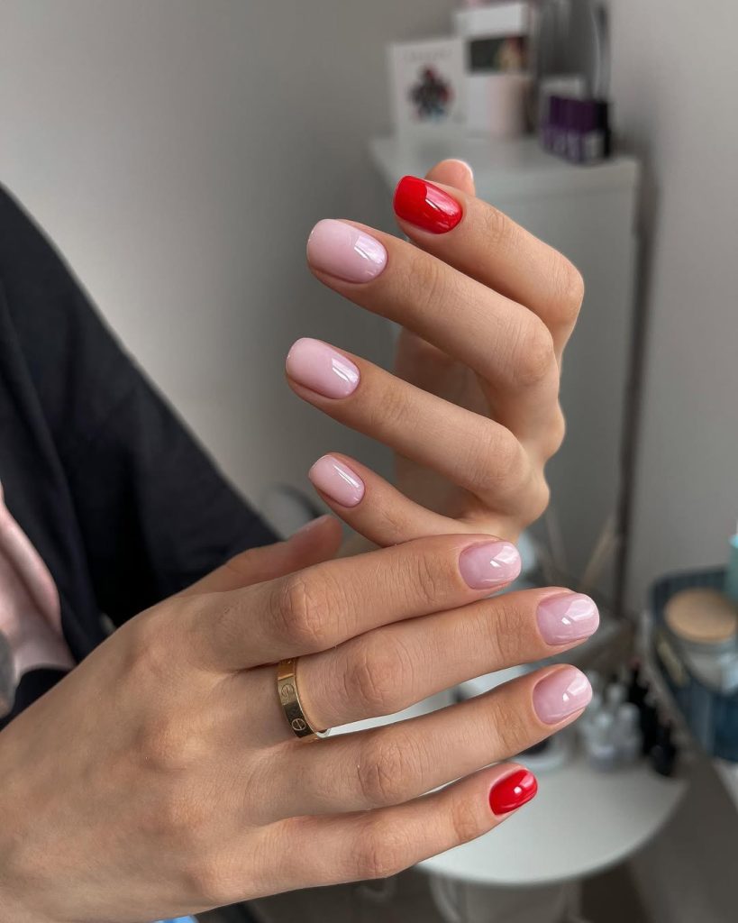 Short oval pink nails with bold red accent fingers creating a striking spring old money combination with high-gloss finish
