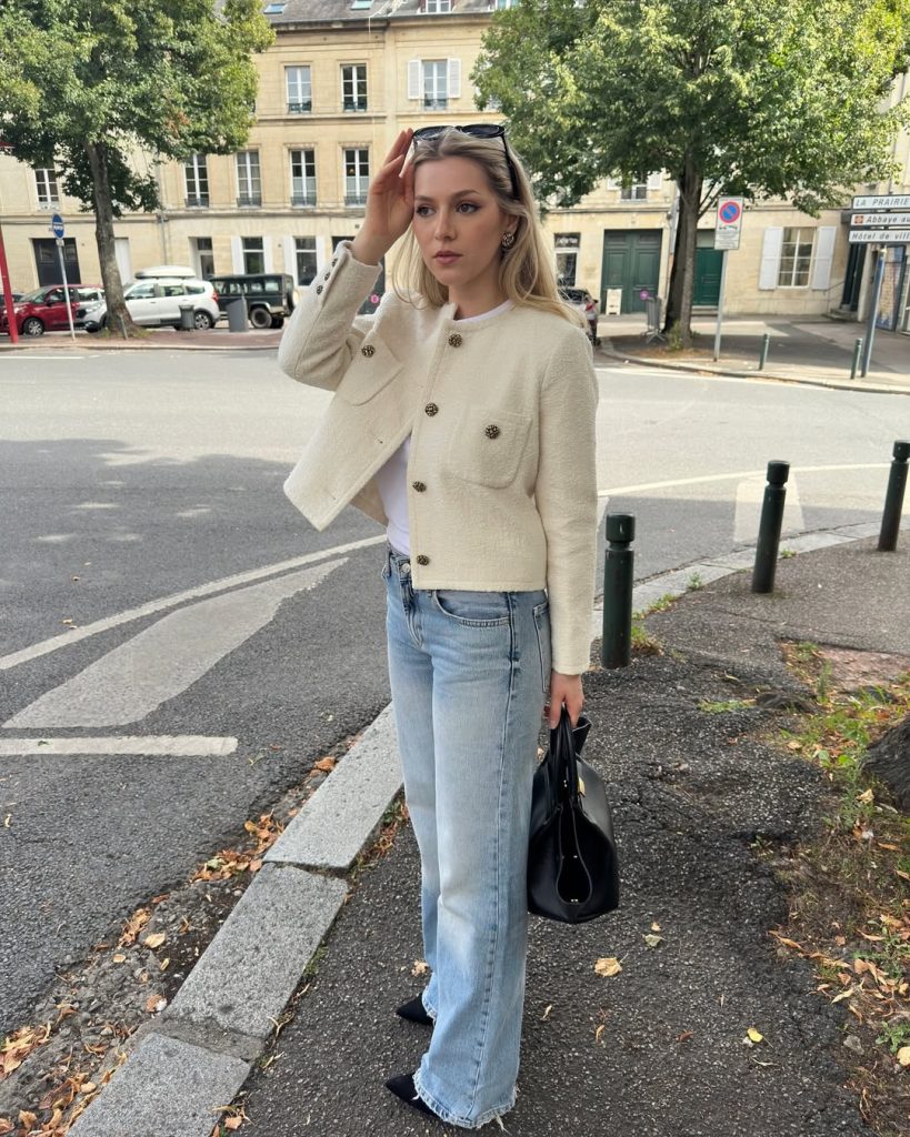 Chic spring outfit with cream boucle jacket, white t-shirt, bootcut jeans and black structured bag
