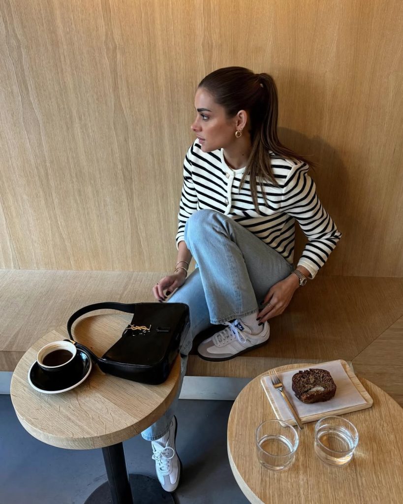 Casual spring outfit featuring a classic black and white striped cardigan, light wash straight-leg jeans, white retro sneakers, small black structured handbag
