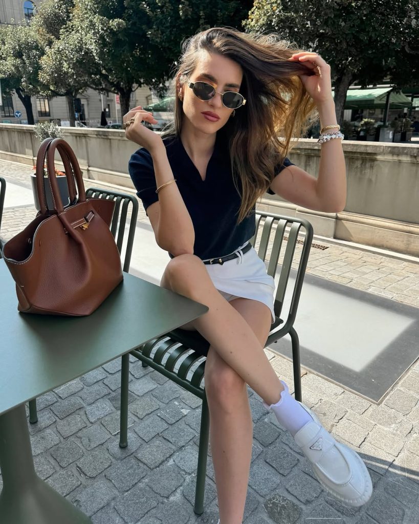 Classy outfit with navy polo top, white tailored skirt, thin black belt, white platform loafers, brown leather handbag and oval sunglasses
