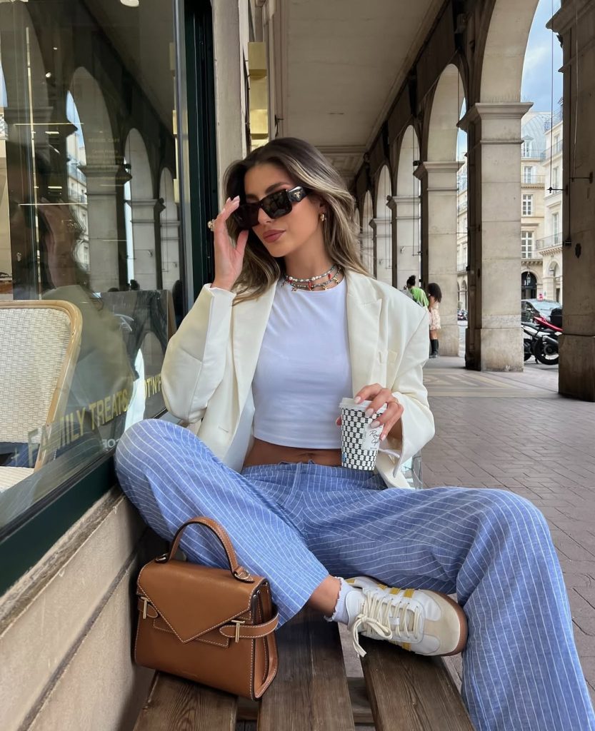Casual spring outfit featuring an oversized cream blazer, white fitted crop top, light blue pinstriped wide-leg pants, retro white sneakers, brown structured handbag
